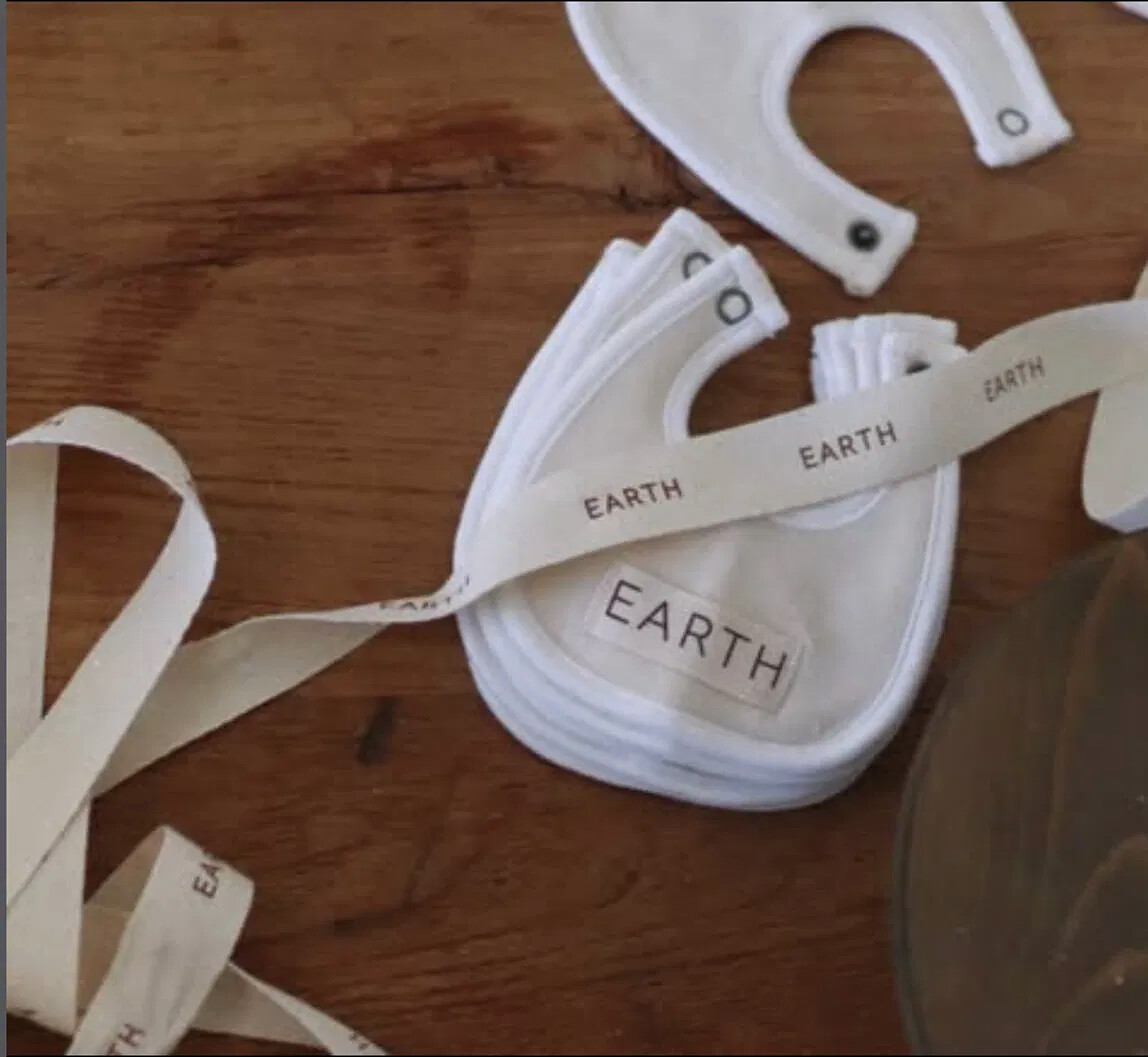 Terry bibs on a worn wooden table, bound with cotton twill tape printed EARTH, EARTH, EARTH.