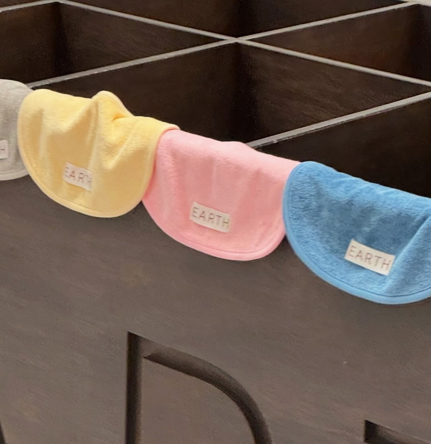 Yellow, pink and blue terry bibs draped over the edge of a dark cabinet, each tagged EARTH.
